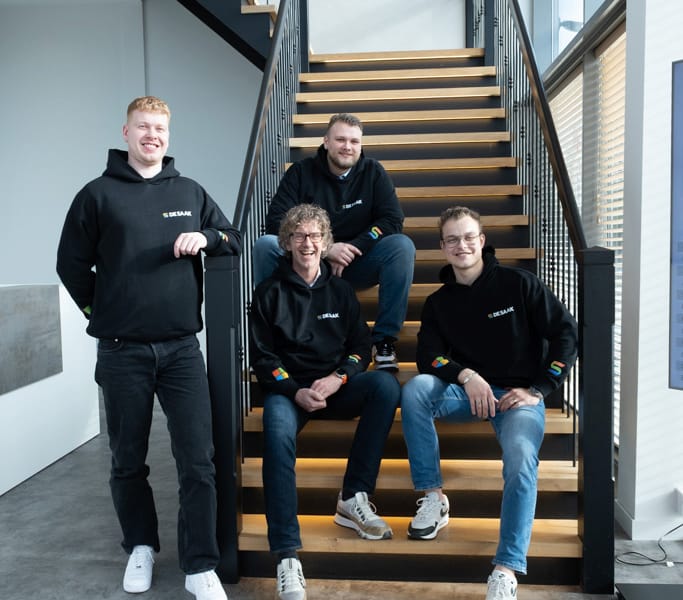 Vier teamleden poseren samen op houten trappen in kantoor